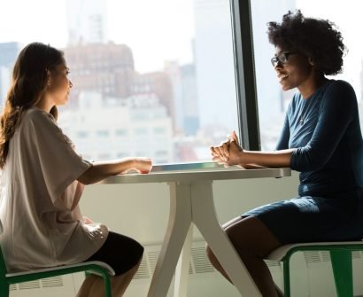 two women sitting beside table and talking