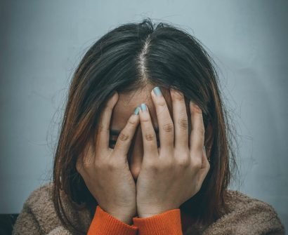 woman in brown sweater covering her face with her hand